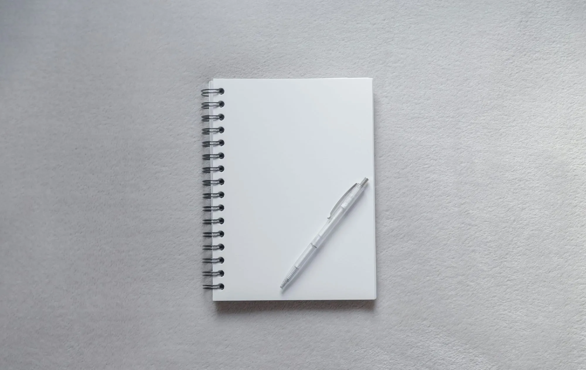 Weißes Notizbuch mit Stift auf hellem Grund